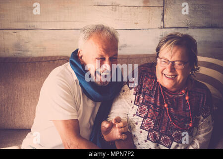 Älterer Mann und Frau eine Menge Spaß zu Hause auf dem Sofa sitzen. Beide lachen zusammen. Home life Konzept. Braun und warme Farben. Stockfoto
