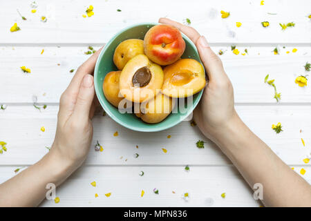 Weiße Schiff deck Tischplatte mit weiblichen Händen hält eine Schüssel mit Aprikosen/Marillen Stockfoto