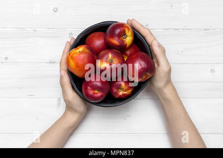 Tischplatte Szene weiblicher Hände halten einen schwarzen Schale mit frischem Nektarine Stockfoto