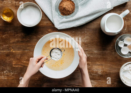 7/8 Schuß von Frau vorbereiten Zutaten zum Backen von Pfannkuchen mit Sieb von Mehl in der Hand Stockfoto