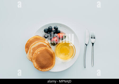 Blick von oben auf die Pfannkuchen mit Beeren und Ahornsirup auf weißen Tisch Stockfoto