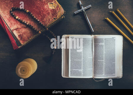 Blick von oben auf die offene Bibel mit Kreuz und Rosenkranz auf dem Tisch Stockfoto