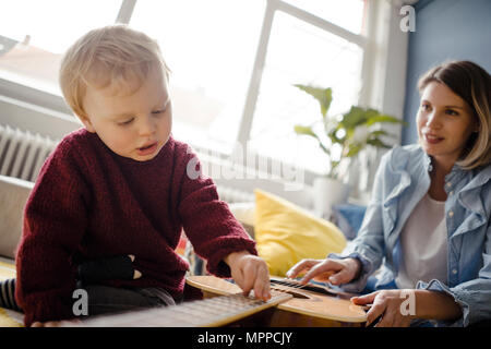 Baby Boy erforschen eine Gitarre mit seiner Mutter Stockfoto