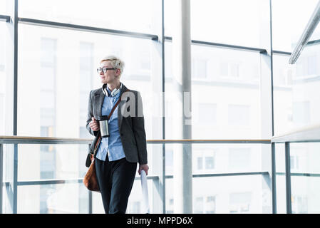 Geschäftsfrau mit Takeaway cup stehen in Bürogebäude an der Glasfront Stockfoto