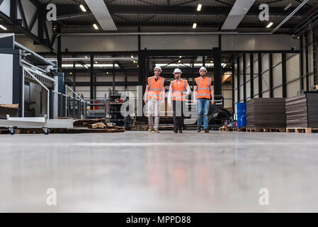 Drei Männer Tragen von Schutzhelmen und Warnwesten zu Fuß auf Factory Shop Boden Stockfoto