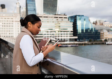 UK, London, Geschäftsfrau auf Brücke über Mobiltelefon Stockfoto