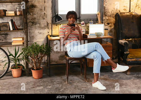 Junge Frau vor einem Schreibtisch in einem Loft mit Handy sitzen Stockfoto