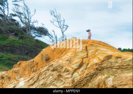 Pacific City, Oregon, USA - 13. September 2015: eine junge Frau in einem langen Kleid mit langen Haaren steht auf einem Sandstein Bluff. Ihr langes Haar und d Stockfoto