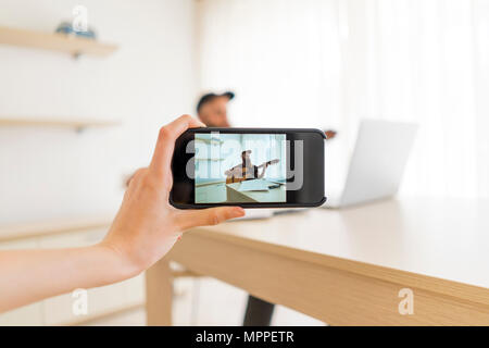 Hand mit Handy unter Bild der Mann spielt Gitarre zu Hause Stockfoto