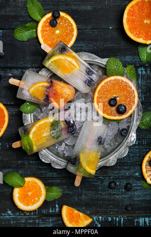 Hausgemachte detox Eis am Stiel mit Blaubeeren, Orangenscheiben und Minze auf schwarzem Holz Stockfoto