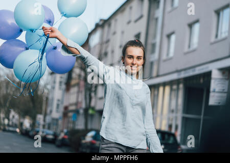 Porträt der lächelnde Frau mit blauen Ballons auf der Straße Stockfoto