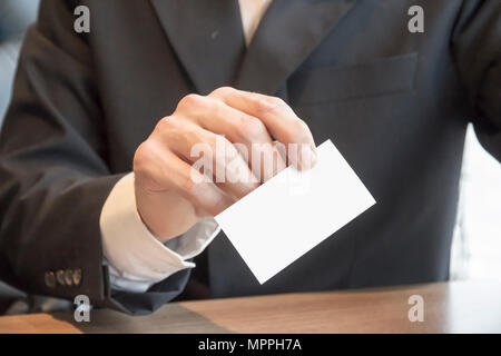 Mann in Anzug auf Tabelle mit leeren weißen Visitenkarte mockup Sitzen Stockfoto