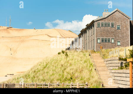 Pacific City Lodging auf einem Hügel von Grass mit einem noch größeren Hügel von Sand im Hintergrund vor einem blauen Himmel und weißen Wolken Stockfoto