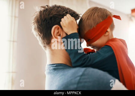 Kleiner Junge verkleidet als ein Superheld auf den Armen seines Vaters Stockfoto