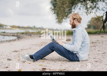 Deutschland, Duesseldorf, Mann sitzt am Strand mit Laptop Stockfoto