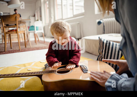 Baby Boy erforschen eine Gitarre mit seiner Mutter Stockfoto