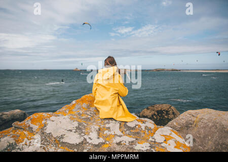 Frankreich, Bretagne, Landeda, Dünen de Sainte-Marguerite, junge Frau sitzt auf Felsen an der Küste Stockfoto