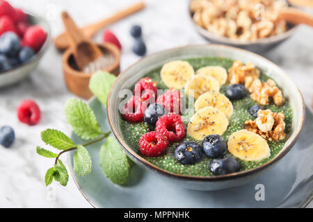 Buddha Schüssel grünem Chia Pudding mit Bananenscheiben, Blaubeeren, Himbeeren und Walnüsse Stockfoto