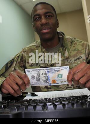 Sgt. Nathaniel Gillens, Informationsspezialist Technologie mit dem 390th Signal-Bataillon 160. Signal Brigade, zeigt eine Rechnung $100 als ein Beispiel für eine die finanziellen Vorteile der bereitgestellten Leben wie Thrift Savings Plan, Kaution Sparprogramm und steuerfreie Erträge im Camp Arifjan, Kuwait, 8. April 2017. April ist National Financial Literacy-Monat. Stockfoto