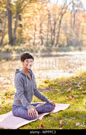 Lächelnd Mitte der erwachsenen Frau im Wald Üben Yoga, Lotus Position Stockfoto