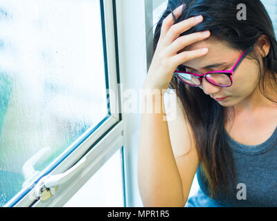 Frau depressiv oder traurig, Frau tragen Brille allein sitzen und über ihr Gesicht wegen einer head Ache in der Nähe der Fenster. Stockfoto