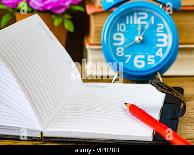 Büro Zubehör einschließlich der roten Bleistift auf Notiz Buch, Stapel von Buch, Rechner, Wecker und rosa Blume auf Holz- Hintergrund. Bildung und Busin Stockfoto