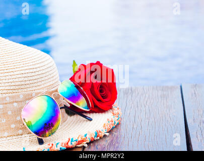 Red rose Blüten mit Sommer Hut und Sonnenbrille am Pool. Urlaub und Entspannung, Sommer Travel Concept. Stockfoto