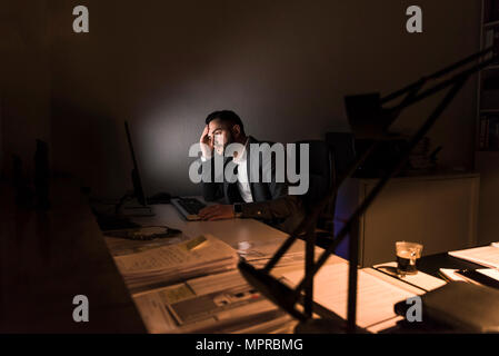 Nachdenkliche junge Unternehmer am Schreibtisch im Büro in der Nacht Stockfoto