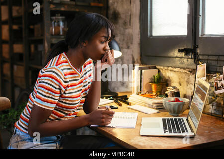 Nachdenkliche junge Frau am Schreibtisch sitzen in einem Loft im Laptop suchen Stockfoto