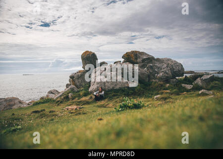 Frankreich, Bretagne, Landeda, Dünen de Sainte-Marguerite, junge Frau an Felsen an der Küste sitzen Stockfoto