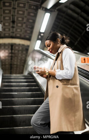 UK, London, Lächeln, Geschäftsfrau, die auf der Rolltreppe der U-Bahnstation an der Zelle Telefon Stockfoto