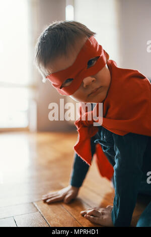 Kleiner Junge verkleidet als ein Superheld kauern auf dem Boden zu Hause