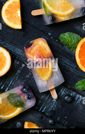 Hausgemachte detox Eis am Stiel mit Blaubeeren, Orangenscheiben und Minze auf schwarzem Holz Stockfoto