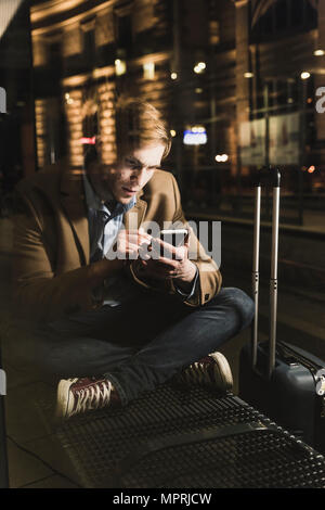 Geschäftsmann mit Mobiltelefon an Straßenbahn-Station bei Nacht Stockfoto