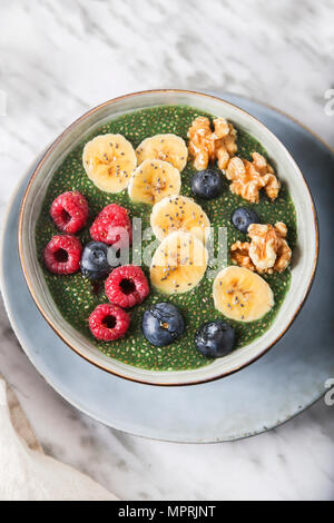 Buddha Schüssel grünem Chia Pudding mit Bananenscheiben, Blaubeeren, Himbeeren und Walnüsse Stockfoto