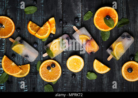 Hausgemachte detox Eis am Stiel mit Blaubeeren, Orangenscheiben und Minze auf schwarzem Holz Stockfoto