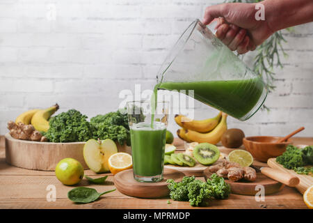Mann mit Glas umgeben von grünen Smoothie Zutaten Stockfoto