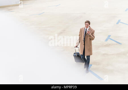 Geschäftsmann mit rollenden Koffer und Smartphone wandern in der Parkgarage Stockfoto