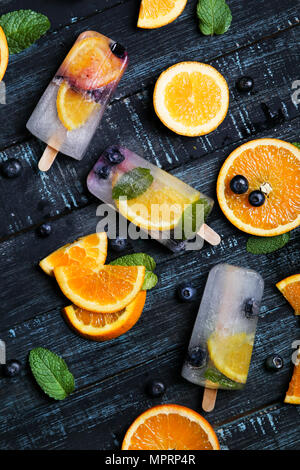 Hausgemachte detox Eis am Stiel mit Blaubeeren, Orangenscheiben und Minze auf schwarzem Holz Stockfoto