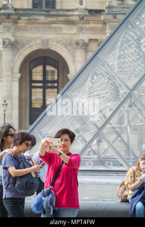 Eine chinesische Frau touristische Tun selfie vor dem Louvre und Pyramide, Paris, Frankreich Stockfoto