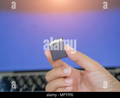 Closeup Hand, die eine Speicherkarte mit Laptop Hintergrund. Stockfoto