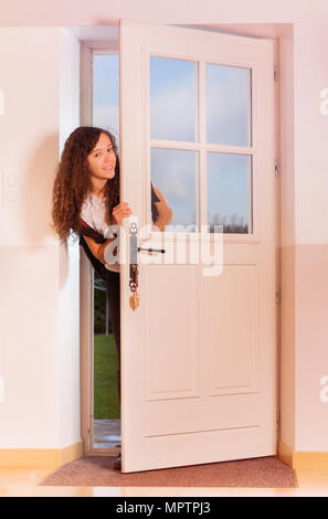 Cute curly Jugendmädchen schauen durch die vordere Tür, wieder von der Schule nach Hause Stockfoto