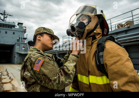 SPC. Angelina Utanes, ein US Army Reserve Wasserfahrzeug Betreiber Soldat mit dem 949th Transport-Unternehmen unterstützt Spc. Huy Dinh mit anziehen Brandbekämpfung Anzug und Maske für eine Reihe von Porträts und Bilder darstellen ihre militärische Besetzung Spezialität bei einem Fotoshooting, die an Bord eines Logistik-Unterstützung-Schiffes in Baltimore, Maryland, am 7. und 8. April 2017 stattfand. (Foto: US Army Reserve Master Sgt. Michel Sauret) Stockfoto