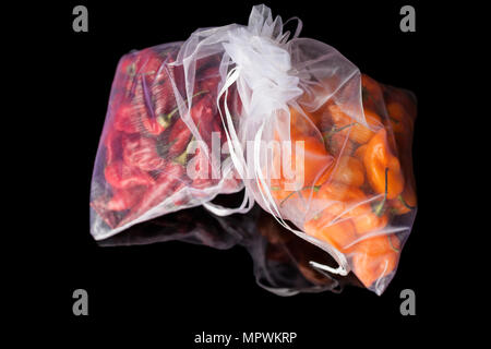 Zwei weiße Gas transparente Säcke mit kleinen orange und rote habanero Paprika auf schwarzem Hintergrund mit Reflektion Stockfoto