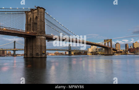 Die Brooklyn Bridge als Sonnenuntergang mit der Manhattan Bridge im Hintergrund span eine ruhige East River. Stockfoto