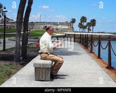 Der Mensch nutzt sein Smartphone, während auf einer Bank entlang der Matanzas Bay in St. Augustine, Florida, USA, 2018, © katharine Andriotis Stockfoto