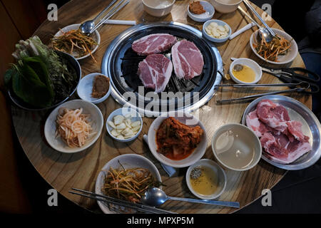 Ein klassischer koreanischer Grillaufstrich rund um einen Tischgrill, auf dem die Gäste verschiedene Fleischstücke zubereiten, begleitet von einer Auswahl an gemeinsamen Beilagen, die als Banchan bekannt sind. Serviert in einem Restaurant auf dem Gwangjang Market in Seoul. Südkorea Stockfoto