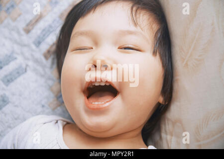 Close-up von verspielten Mädchen mit offenem Mund winking, während am Bett zu Hause liegen Stockfoto