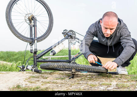Mann Reparatur Fahrrad auf Feld am Bauernhof gegen den klaren Himmel Stockfoto