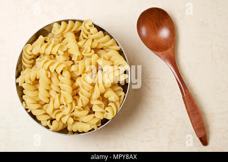 Ansicht von oben ungekochten rotini Pasta in Behälter mit Löffel aus Holz auf Tisch Stockfoto